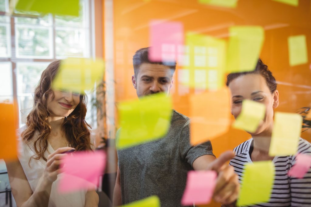 Des cadres d'entreprise lisent des notes autocollantes sur un tableau blanc, lors d'une séance de brainstorming sur la communication autour de la RSE.