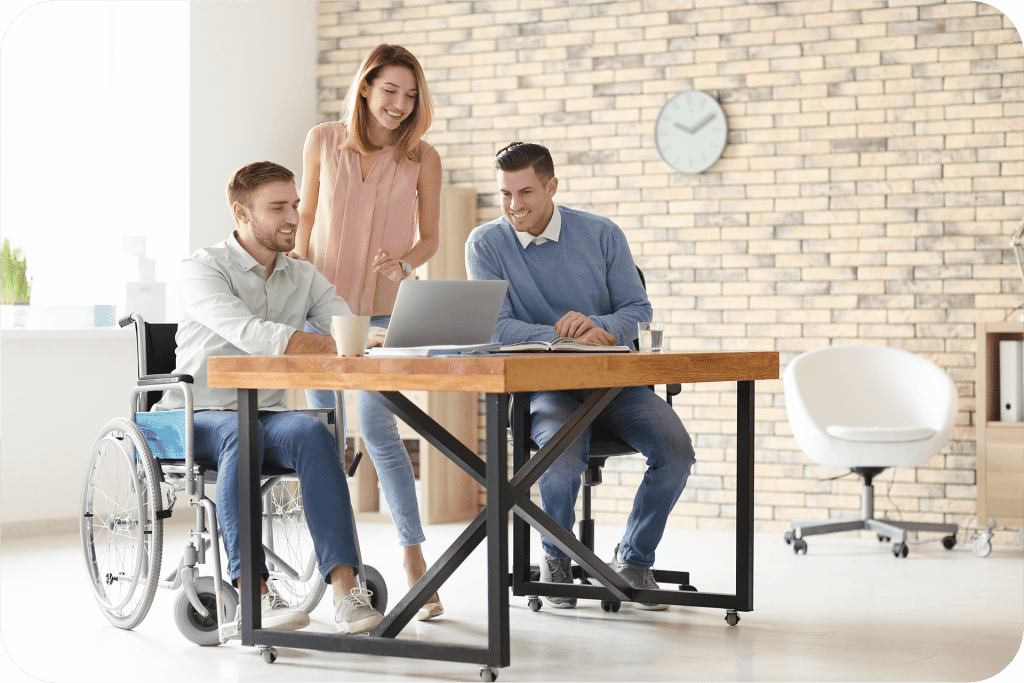 Handicapped man in a wheelchair working on a computer with two coworkers